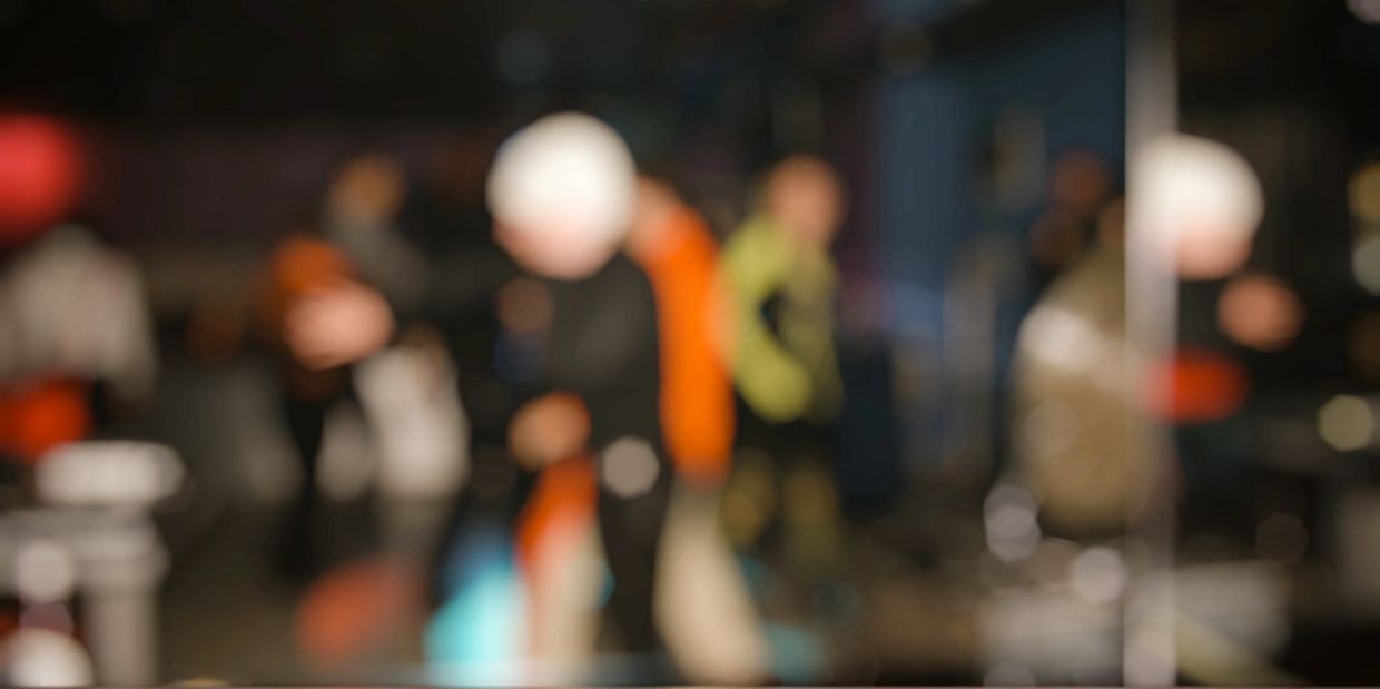 Blurred background of people in a dimly lit indoor setting with reflective floor.