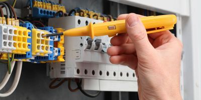 Hand using a voltage tester on an electrical panel.