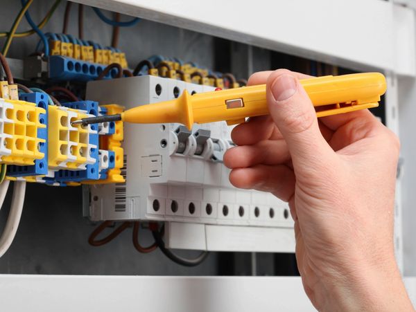 Hand using a voltage tester on an electrical panel.