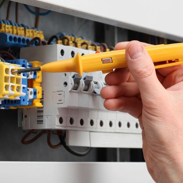Hand using a voltage tester on an electrical panel.
