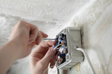 Hands working on wiring inside an electrical junction box.