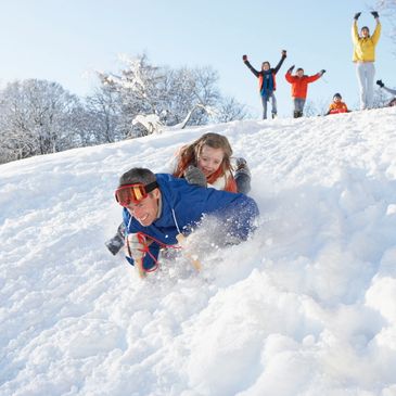People joyfully sledding down a snowy hill on a bright winter day.