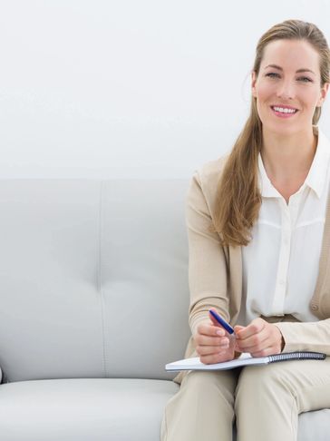 Smiling woman sitting on a couch with a notebook and pen.