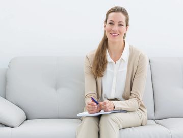 Smiling woman sitting on a couch with a notebook and pen.