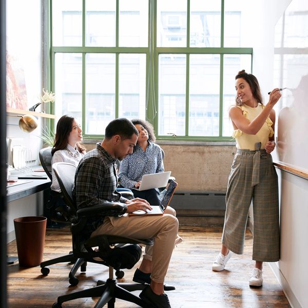 A woman presents ideas on a whiteboard to colleagues in a modern office.
