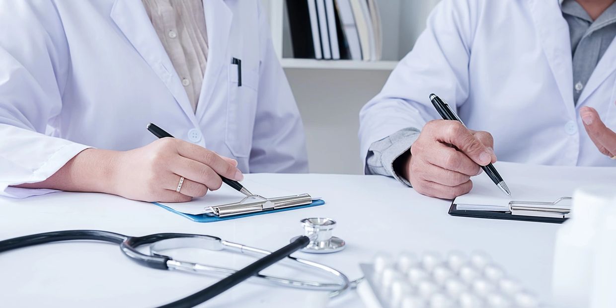 Two doctors in white coats writing on clipboards with medical tools on the table.
