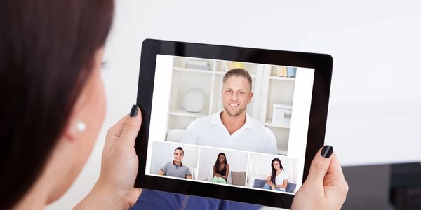 Person holding a tablet during a video conference with four participants.