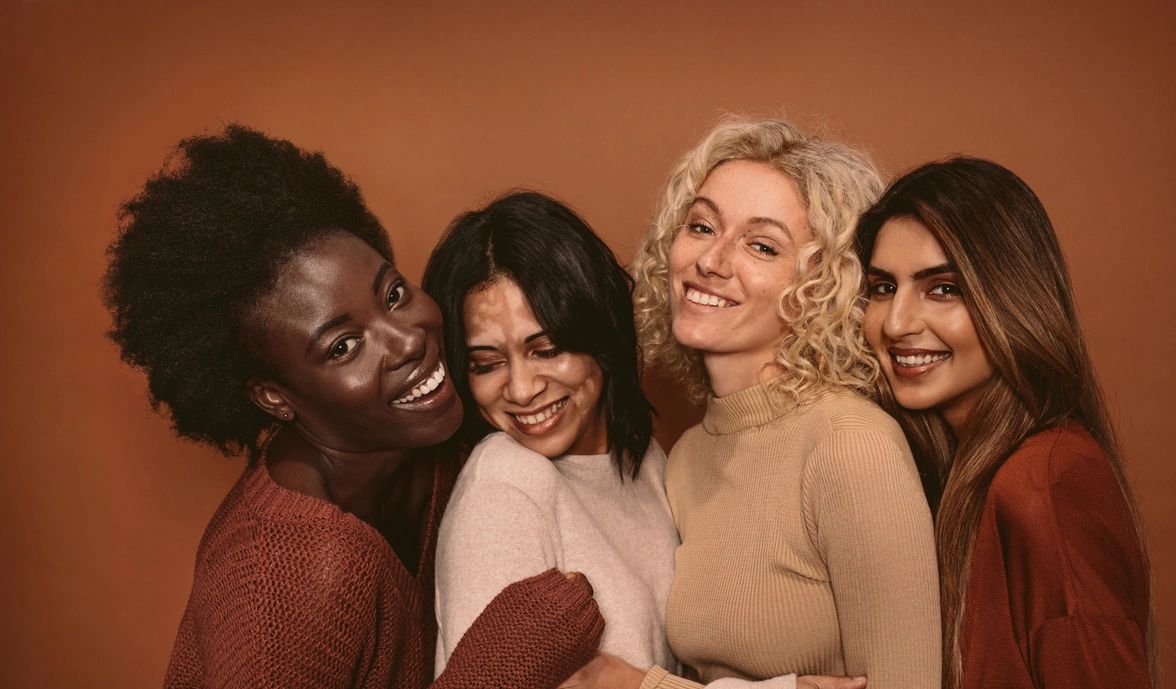 four (4) beautiful, multi-cultural women embracing dressed  in colors of reds and browns