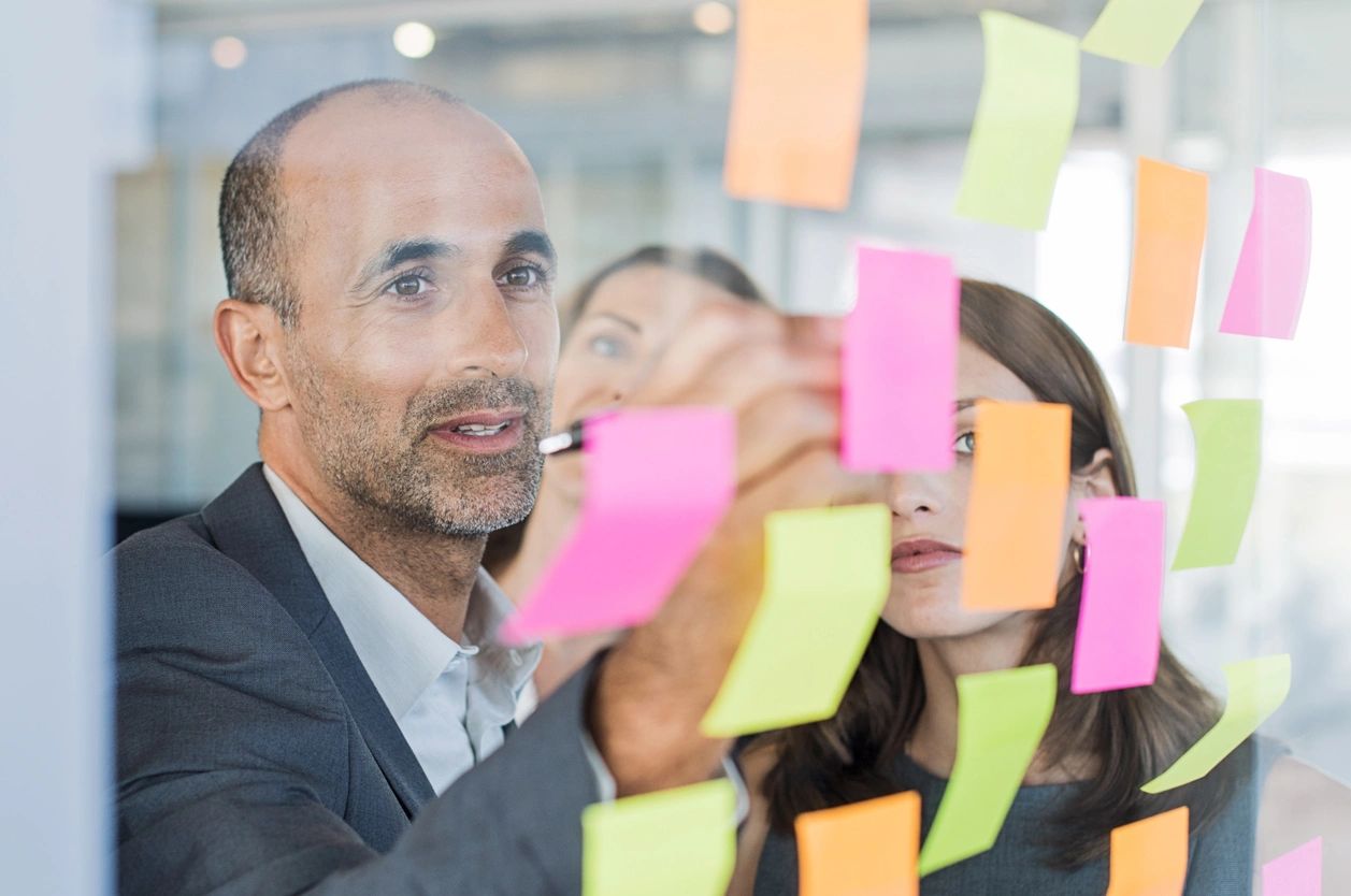 A team discusses their ideas as they make notes on many post-it notes on a office glass window.