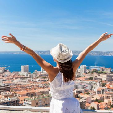 Woman with open arms facing city with blue ocean view and blue skies