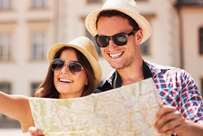 A couple, smiling and happy, whilst holding a map and wearing sunglasses