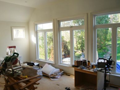 Room under renovation with tools, wooden planks, and large windows.