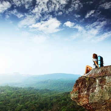 A woman carrying a travel bag while sitting on the cliff of the mountain 