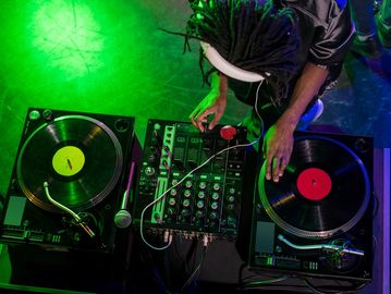 DJ mixing music with turntables and mixer under green lighting.
