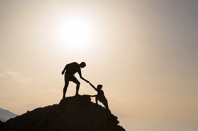 One person helping another to a mountaintop