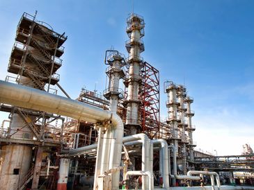 Industrial refinery with tall distillation columns and extensive piping under a clear sky.