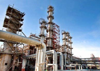 Industrial refinery plant with multiple towers and pipelines under a clear blue sky.
