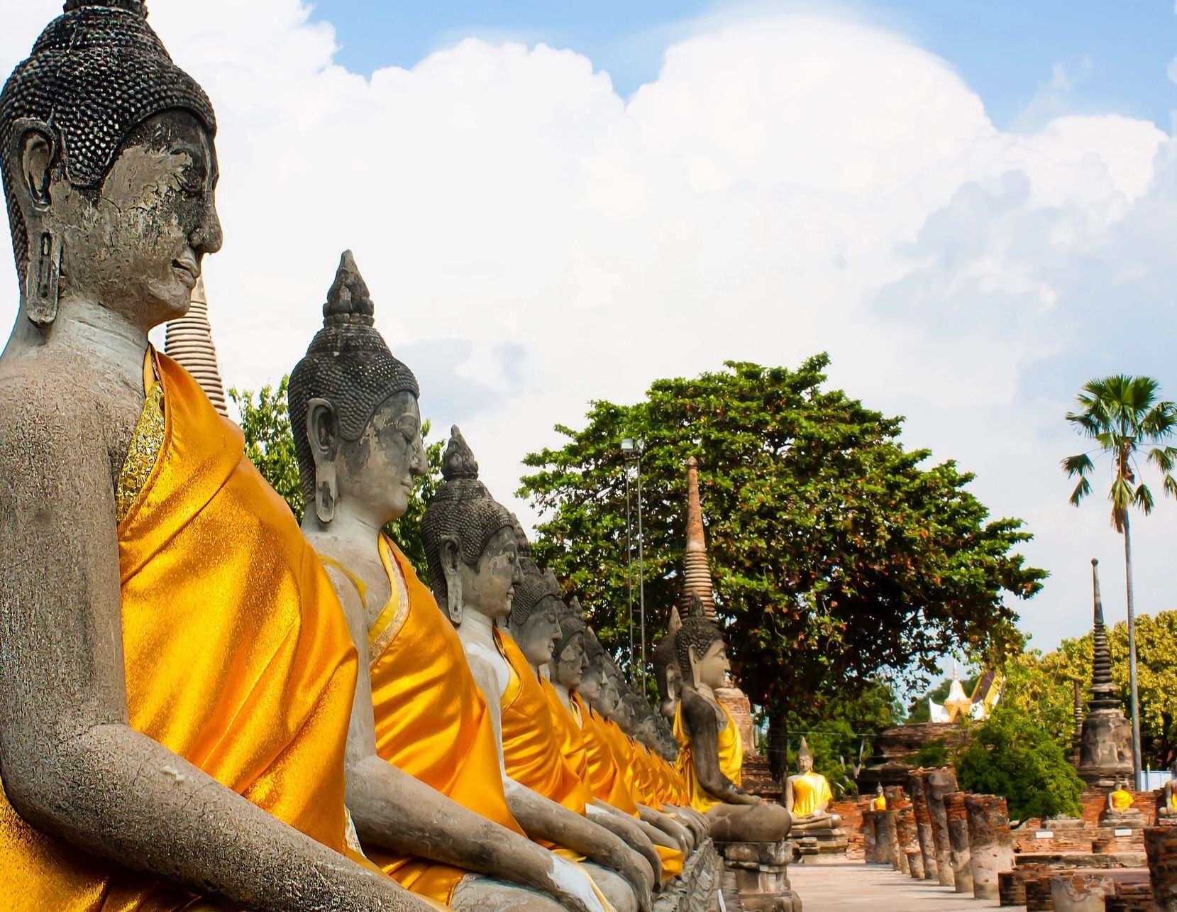 Row of Buddha statues draped in vibrant orange robes at a temple.
