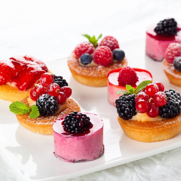 Assorted berry-topped mini tarts and mousse desserts on a white platter.