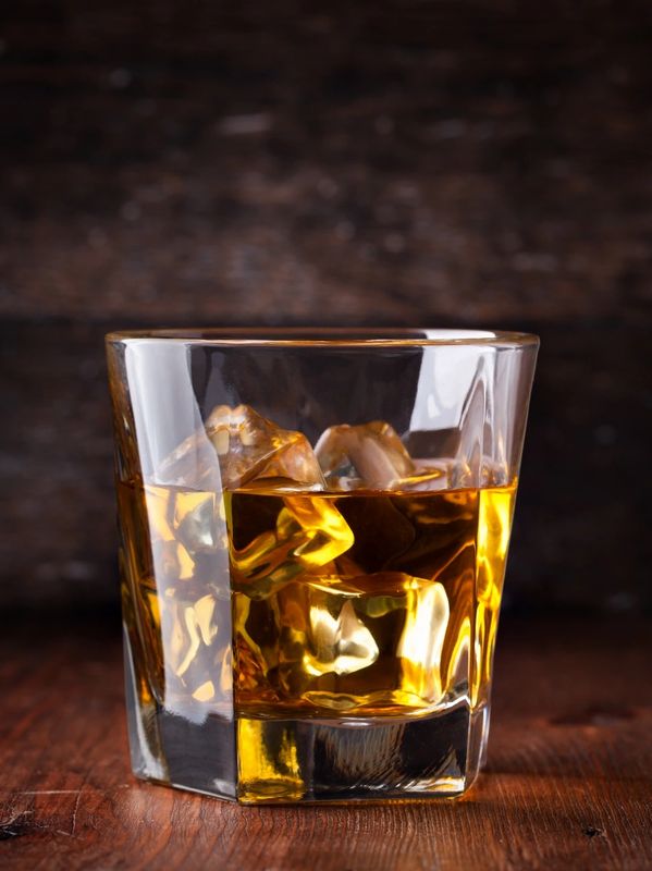 Glass of whiskey with ice on wooden surface.