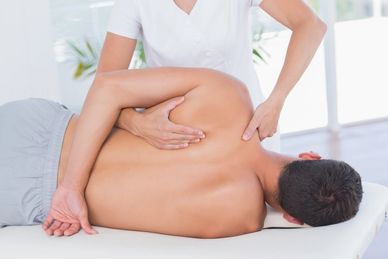 Therapist performing shoulder and back massage on a male client.