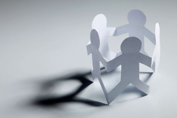 Paper cutouts of people holding hands in a circle casting shadows.