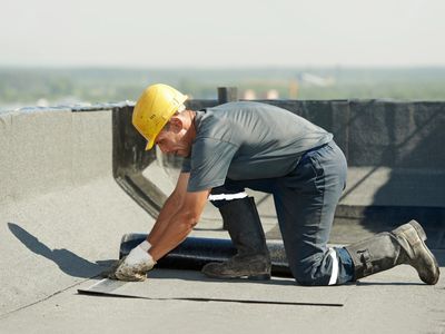 Construction worker installing roofing material on a flat roof.