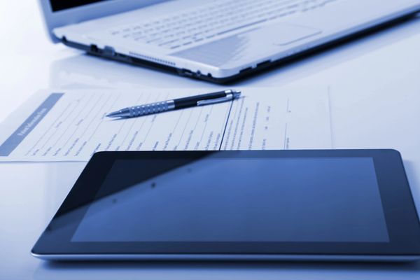 Tablet, pen, and laptop on a reflective white desk.