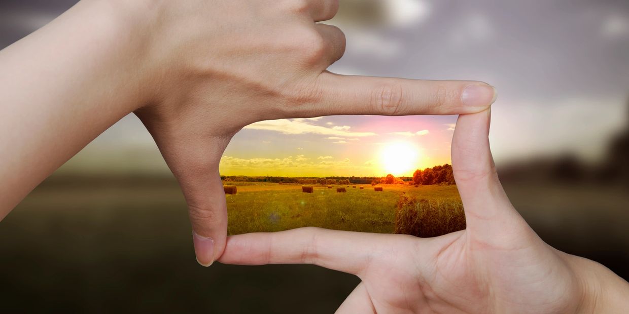 Finger viewfinder with sun and hay bales in a field