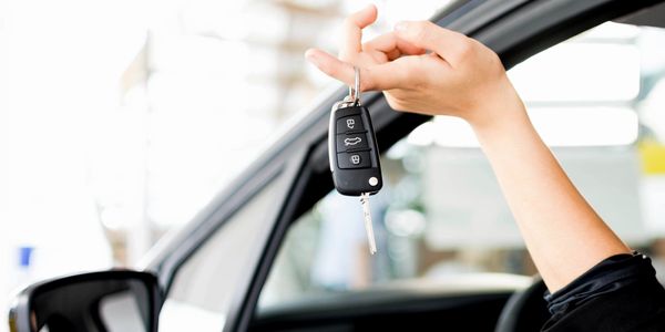 A person holding car keys with one finger through the keyring out the window of a car