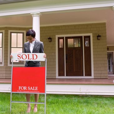 Smiling female adding a sold sign to yard sign in front of the porch of a house