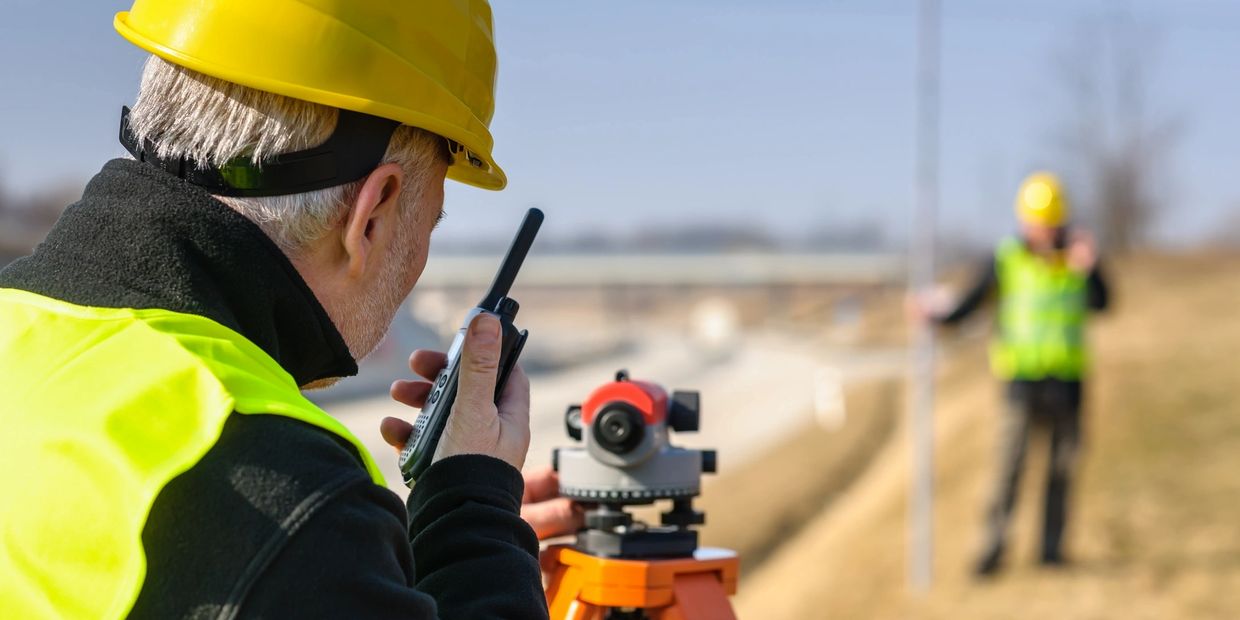 Two construction workers using surveying equipment on site.