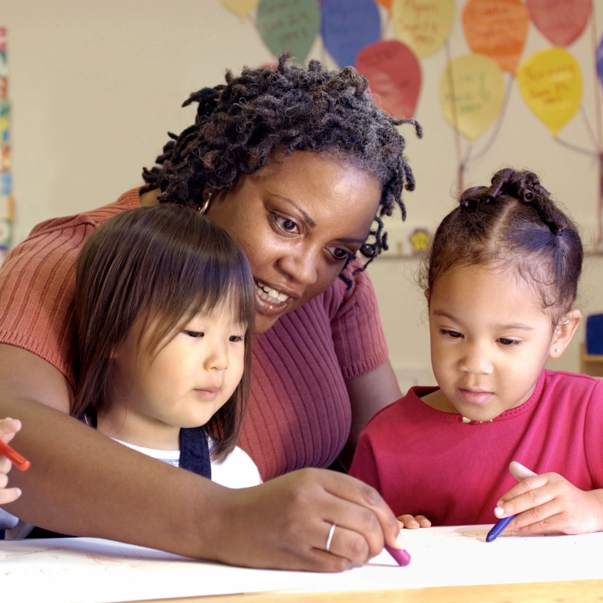 Childcare teacher completing an art activity with two female children.