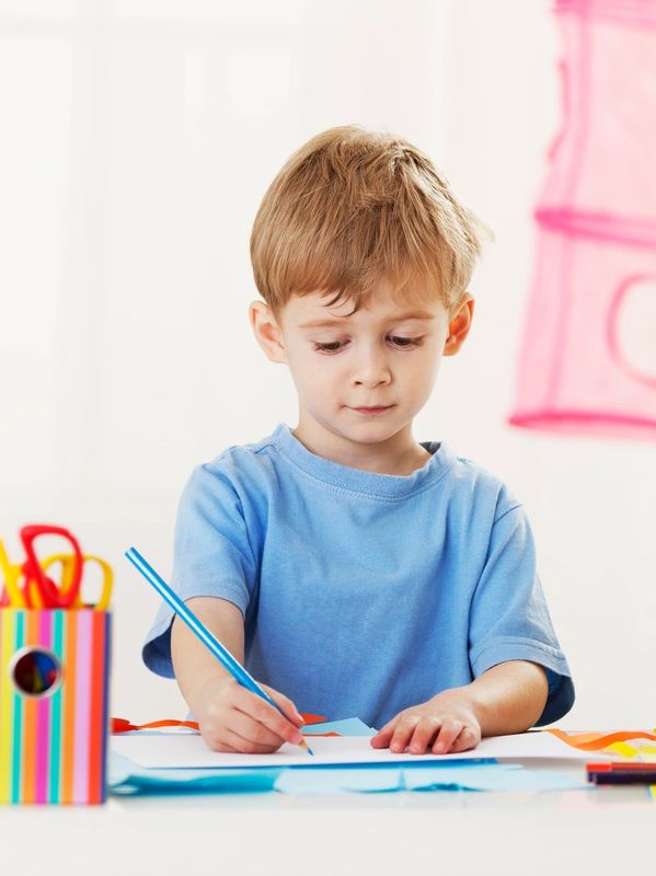 Young boy focused on drawing at a table with colorful supplies.