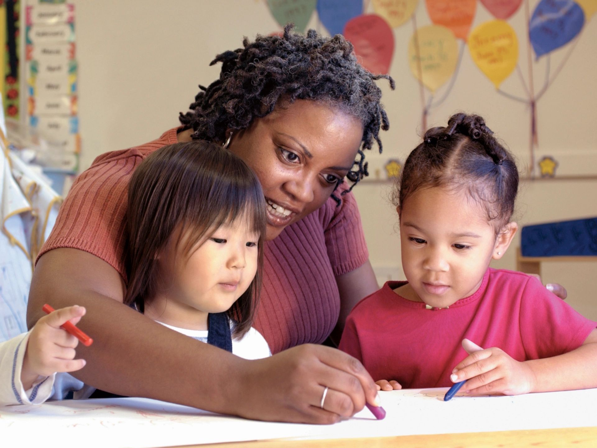 Woman assisting two children to use crayons