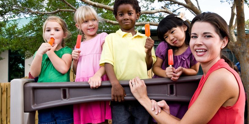 A group of children and a woman enjoying orange popsicles outdoors.