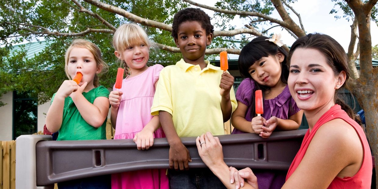 A group of children and an adult enjoying orange popsicles outside.