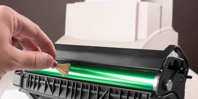 closeup of a hand with a small brush cleaning the roller of a toner cartridge drum roller
