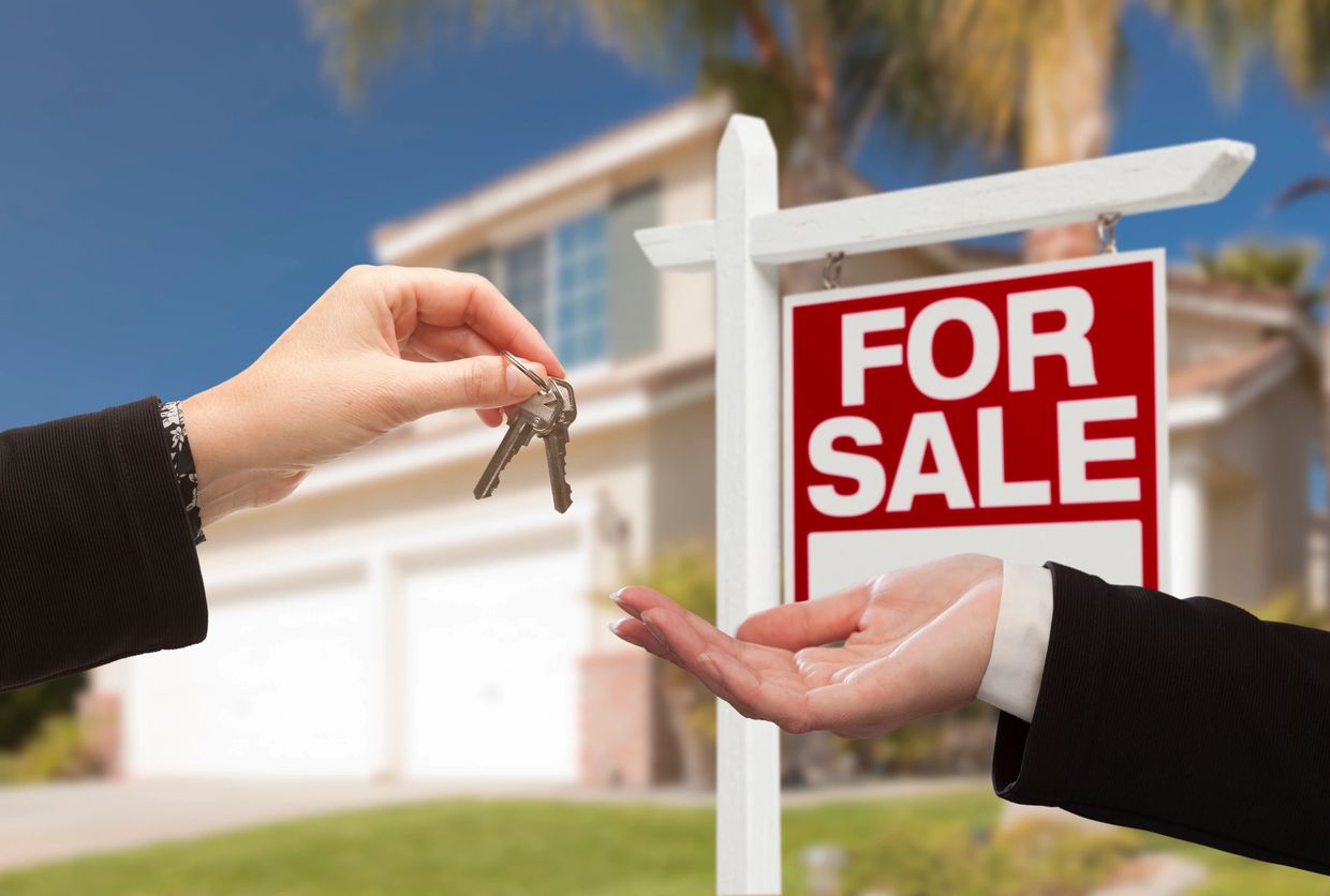 Handing over house keys in front of a for sale sign and home.