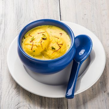 Blue bowl with creamy yellow dessert and saffron strands, served with a matching spoon.
