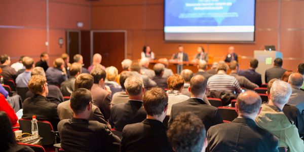 People seated at a conference with a group of speakers seated in front of them