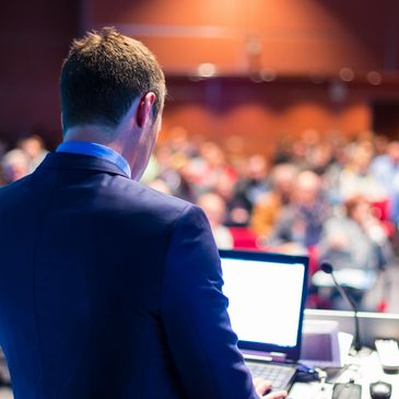 Man in suit presenting to an audience using a laptop.