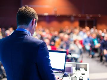 Man in suit presenting to a large audience with a laptop.