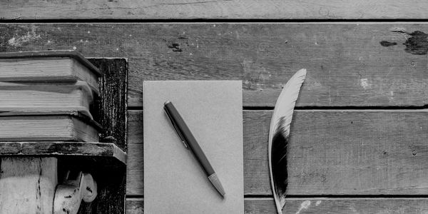 Stack of books, pen on a notebook, and a feather on rustic wooden surface.