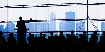silhouette of speaker in front of an audience with skyscrapers in background