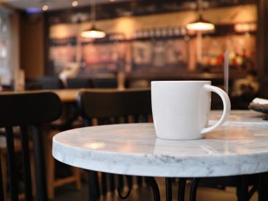 A white mug on a marble table in a cozy cafe setting.