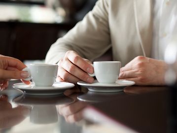 Two people holding small coffee cups at a table.