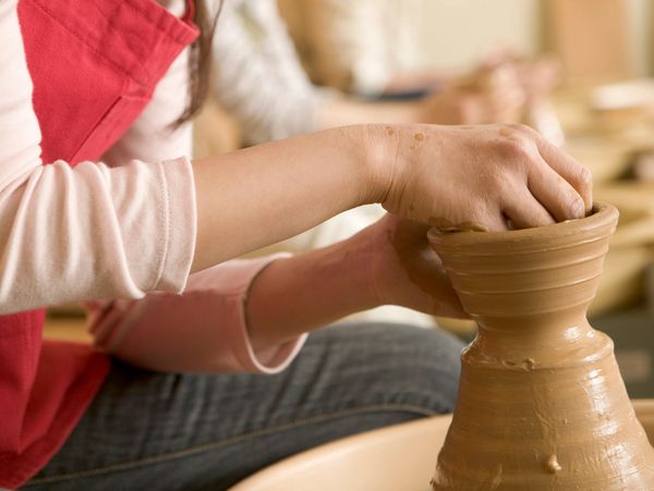 Person shaping clay on a pottery wheel with hands.