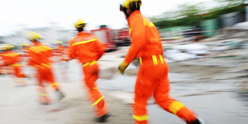 Rescue workers in orange uniforms running urgently at a disaster site.