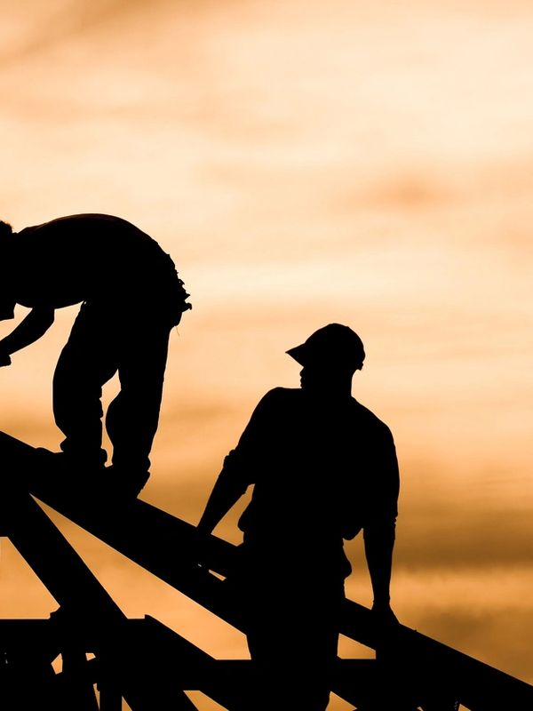 Silhouettes of two construction workers building a wooden structure at sunset.
